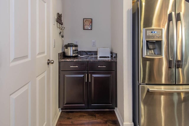 kitchen featuring dark stone counters, dark brown cabinetry, stainless steel fridge, and dark wood-type flooring