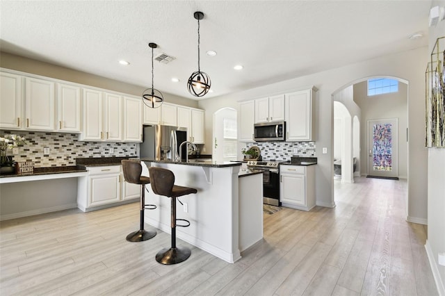 kitchen featuring white cabinetry, stainless steel appliances, decorative backsplash, a center island with sink, and light wood-type flooring