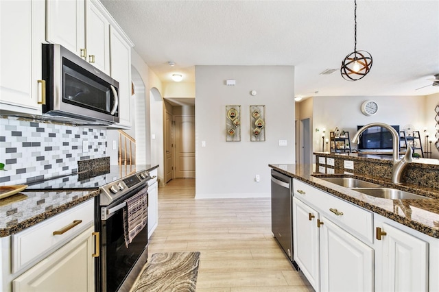 kitchen featuring sink, backsplash, dark stone counters, white cabinets, and appliances with stainless steel finishes