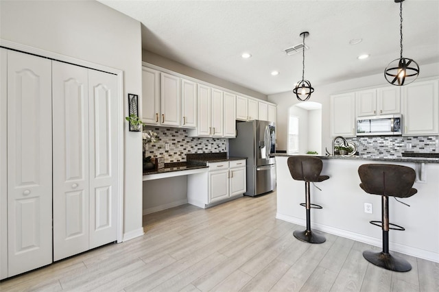 kitchen with decorative light fixtures, white cabinetry, stainless steel appliances, and a breakfast bar