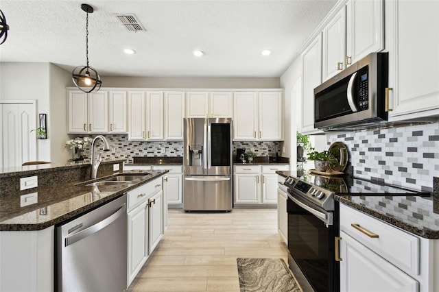 kitchen with sink, dark stone counters, pendant lighting, white cabinets, and appliances with stainless steel finishes