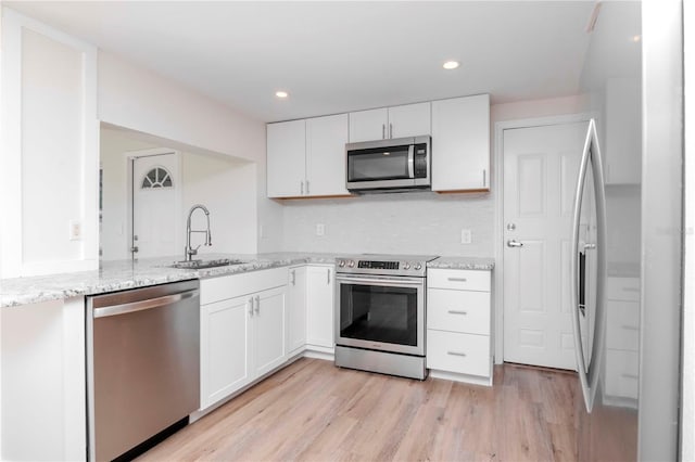 kitchen with white cabinets, appliances with stainless steel finishes, light stone counters, and sink