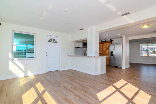 unfurnished living room with a barn door, light wood-type flooring, and sink