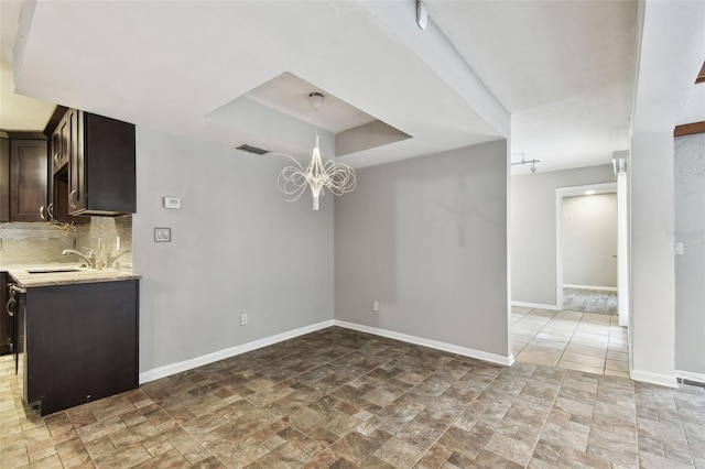 unfurnished dining area with sink, a tray ceiling, and an inviting chandelier