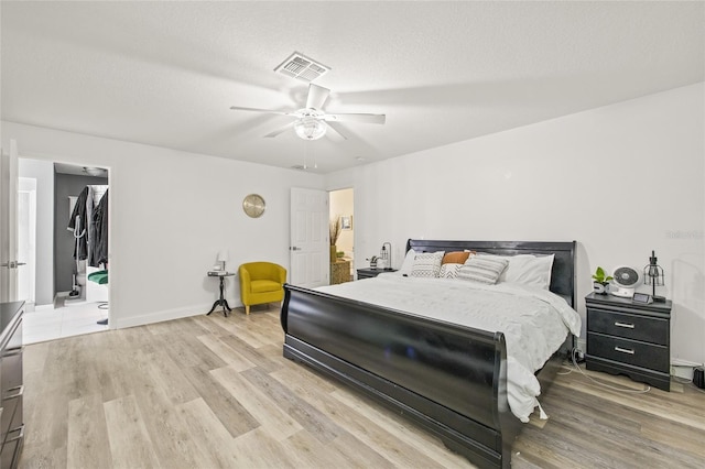 bedroom with a textured ceiling, ceiling fan, light hardwood / wood-style flooring, a closet, and a walk in closet