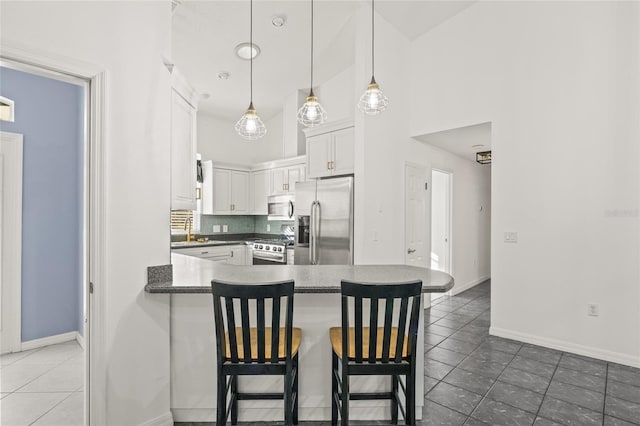 kitchen with decorative light fixtures, white cabinets, a kitchen breakfast bar, decorative backsplash, and appliances with stainless steel finishes