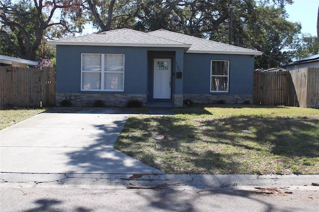 view of front facade featuring stone siding, roof with shingles, fence, a front lawn, and stucco siding