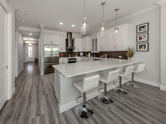 kitchen featuring white cabinetry, a breakfast bar, wall chimney exhaust hood, and stainless steel appliances