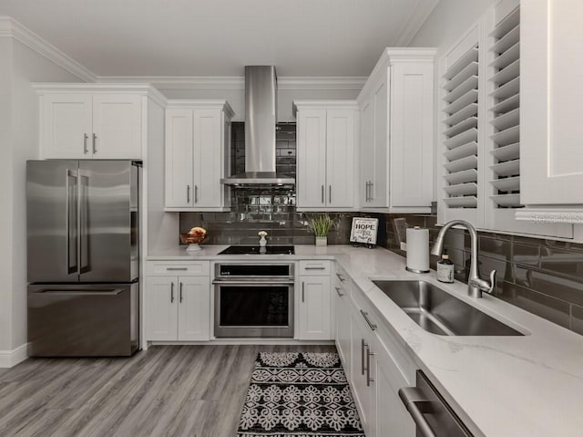 kitchen with white cabinetry, sink, stainless steel appliances, wall chimney range hood, and ornamental molding