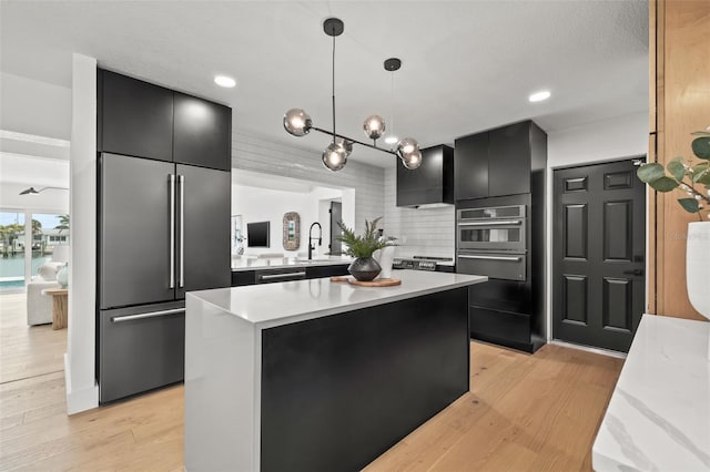 kitchen featuring appliances with stainless steel finishes, decorative light fixtures, a kitchen island, and light wood-type flooring