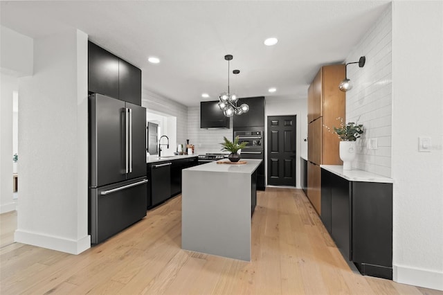 kitchen with appliances with stainless steel finishes, hanging light fixtures, a kitchen island, decorative backsplash, and light wood-type flooring