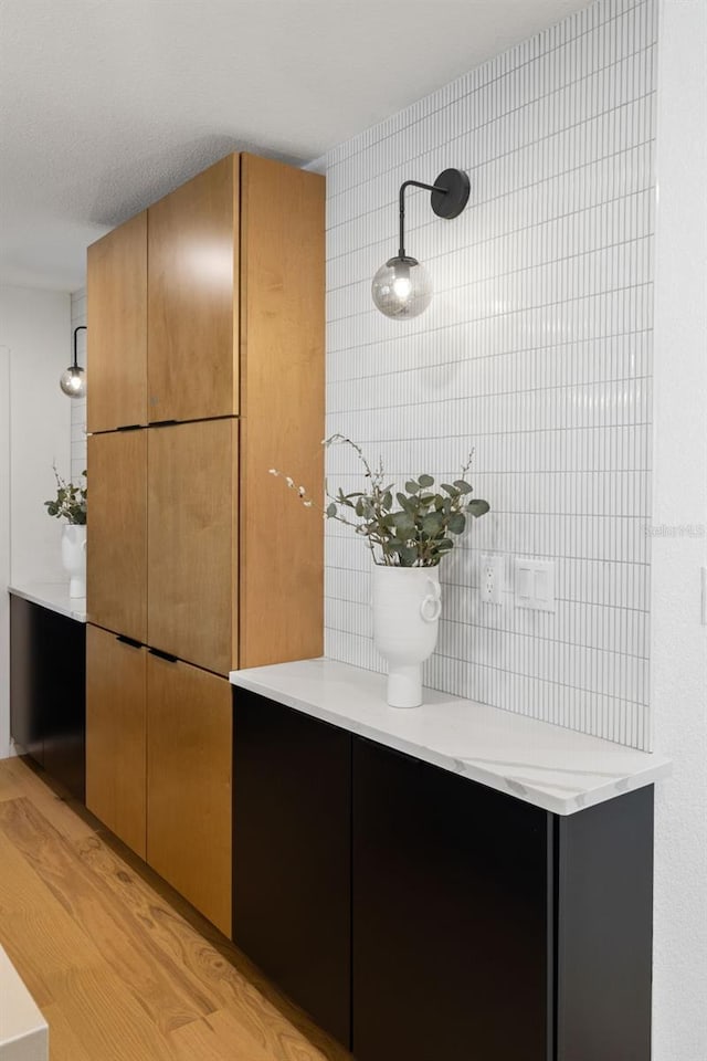 interior space with hanging light fixtures, light stone countertops, tile walls, and light hardwood / wood-style flooring