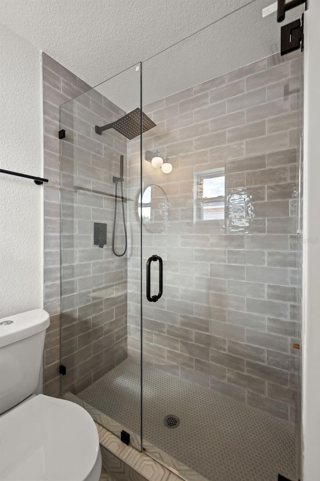 bathroom with toilet, a shower with door, and a textured ceiling