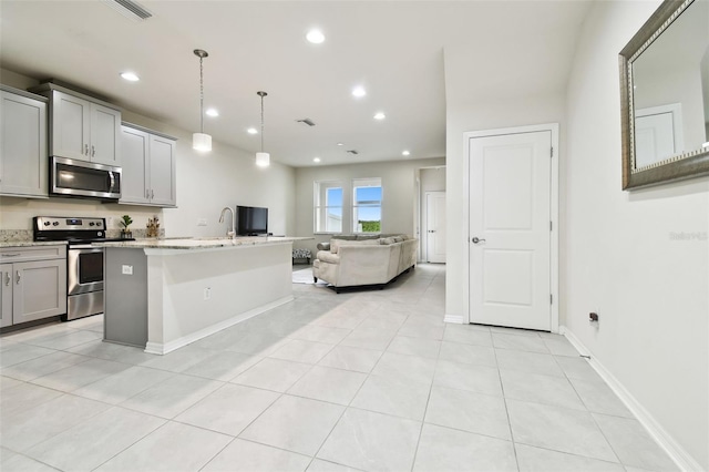 kitchen with light stone countertops, appliances with stainless steel finishes, decorative light fixtures, a kitchen island with sink, and gray cabinetry