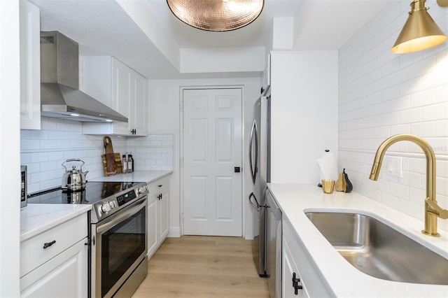 kitchen featuring appliances with stainless steel finishes, white cabinetry, wall chimney exhaust hood, and sink