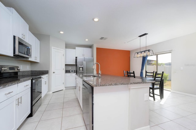 kitchen featuring stainless steel appliances, white cabinets, decorative light fixtures, and a kitchen island with sink