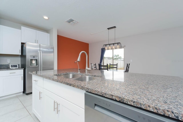 kitchen with stainless steel appliances, light tile patterned floors, light stone counters, sink, and white cabinetry