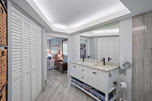 bathroom with a tray ceiling, hardwood / wood-style floors, vanity, and a textured ceiling