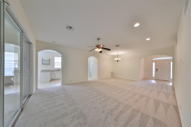 carpeted empty room featuring plenty of natural light and ceiling fan with notable chandelier