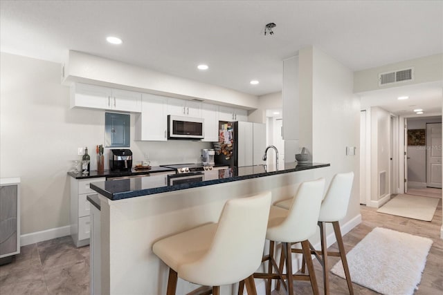 kitchen with kitchen peninsula, white cabinetry, a breakfast bar, and refrigerator