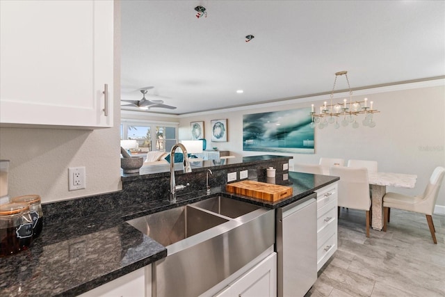 kitchen with white cabinetry, sink, dark stone counters, and ceiling fan with notable chandelier