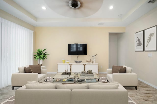 living room featuring a raised ceiling, ceiling fan, plenty of natural light, and light hardwood / wood-style floors