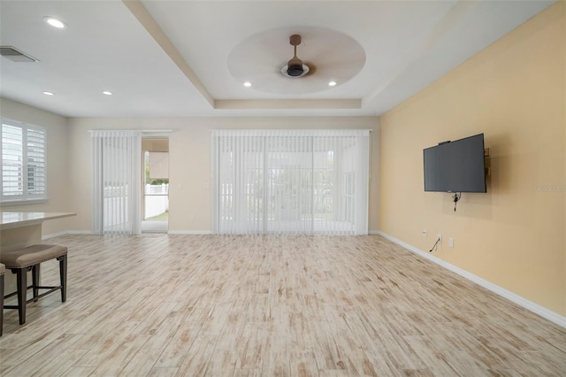 living room featuring ceiling fan, light wood-type flooring, a wealth of natural light, and a tray ceiling