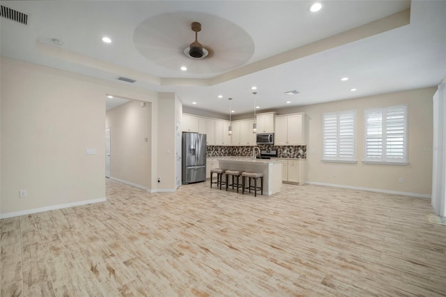 kitchen featuring pendant lighting, a raised ceiling, a breakfast bar, a center island with sink, and appliances with stainless steel finishes