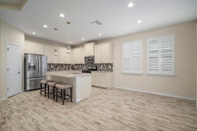 kitchen featuring pendant lighting, stainless steel appliances, backsplash, a center island with sink, and a breakfast bar area