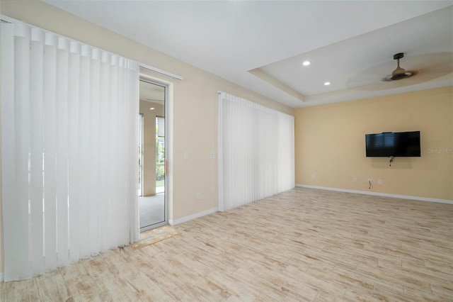 spare room with ceiling fan, a raised ceiling, and light hardwood / wood-style flooring