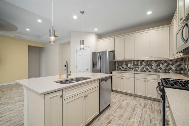 kitchen with appliances with stainless steel finishes, backsplash, a kitchen island with sink, decorative light fixtures, and sink