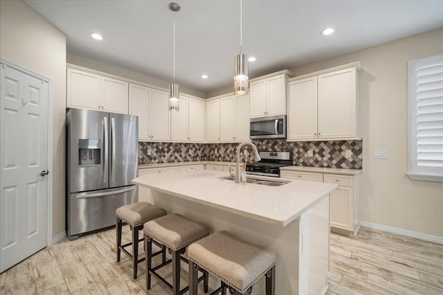 kitchen featuring appliances with stainless steel finishes, a kitchen bar, sink, hanging light fixtures, and a kitchen island with sink