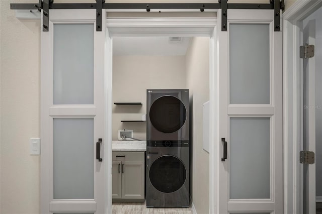 laundry room featuring light hardwood / wood-style floors, cabinets, and stacked washer / dryer