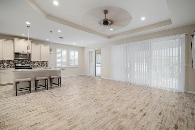 kitchen featuring a kitchen breakfast bar, stainless steel appliances, a tray ceiling, and hanging light fixtures