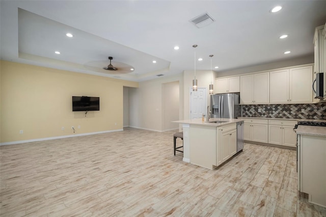 kitchen featuring decorative light fixtures, ceiling fan, a raised ceiling, a kitchen island with sink, and stainless steel appliances