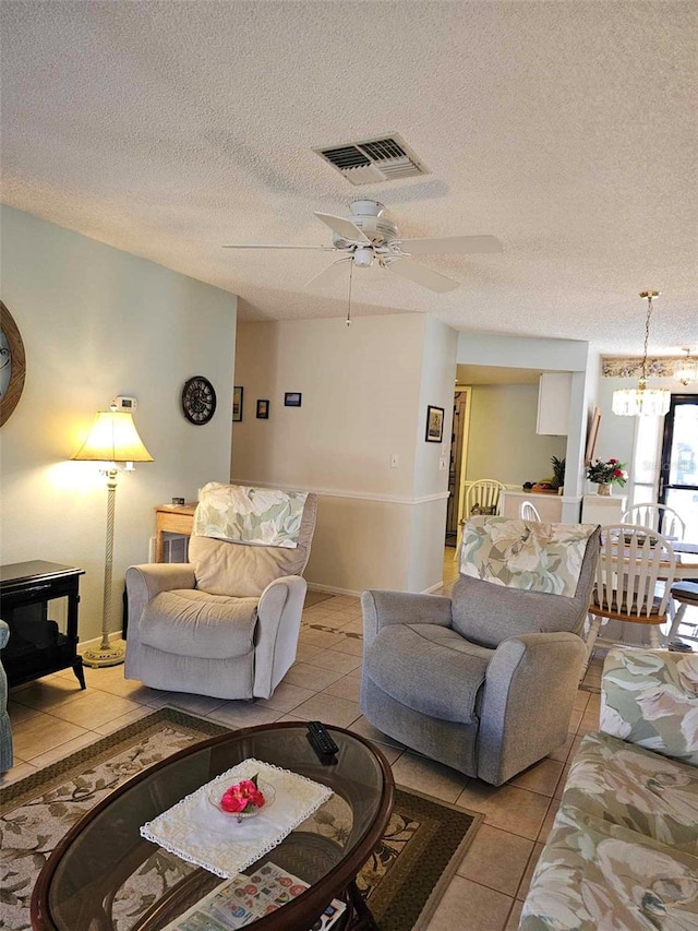 living room featuring ceiling fan with notable chandelier, light tile patterned flooring, and a textured ceiling