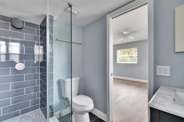 bathroom featuring a tile shower, vanity, a textured ceiling, ceiling fan, and toilet