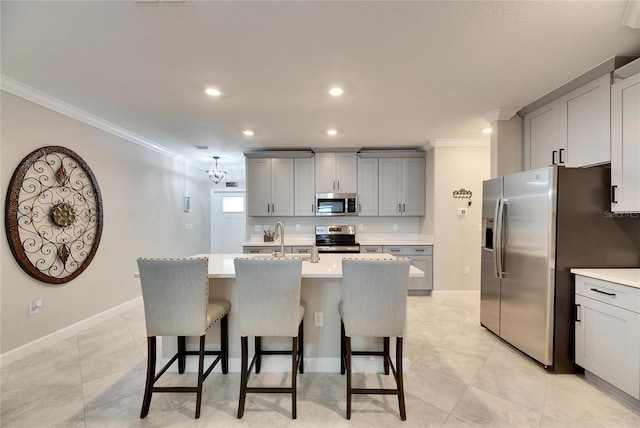 kitchen featuring stainless steel appliances, an island with sink, sink, gray cabinetry, and crown molding