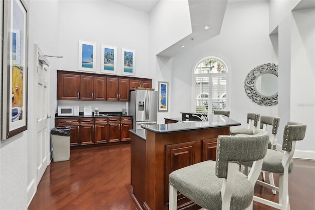 kitchen with a kitchen island with sink, stainless steel refrigerator with ice dispenser, a high ceiling, dark wood-type flooring, and a breakfast bar