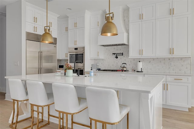 kitchen featuring a center island with sink, decorative backsplash, a kitchen breakfast bar, stainless steel appliances, and white cabinets