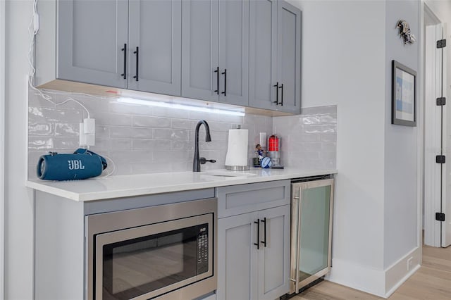 bar featuring stainless steel microwave, light hardwood / wood-style flooring, tasteful backsplash, and sink