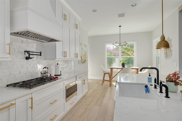 kitchen with decorative light fixtures, white cabinetry, stainless steel gas stovetop, and custom range hood