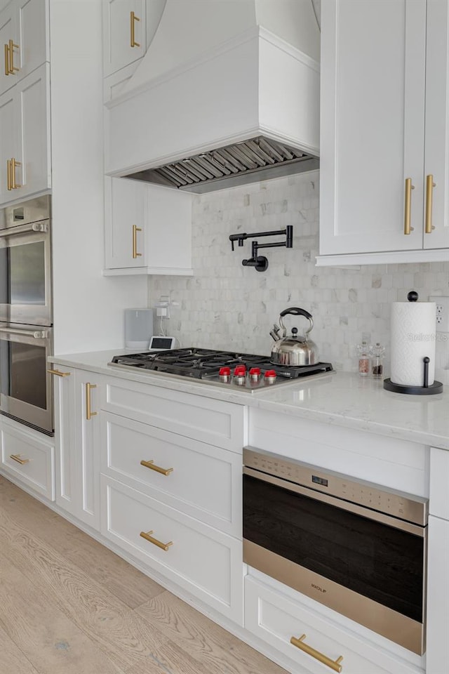 kitchen featuring custom exhaust hood, stainless steel appliances, tasteful backsplash, light stone countertops, and white cabinets