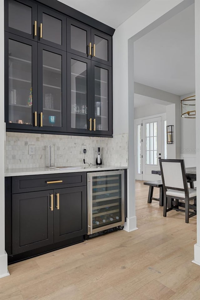 bar with decorative backsplash, wine cooler, and light hardwood / wood-style flooring