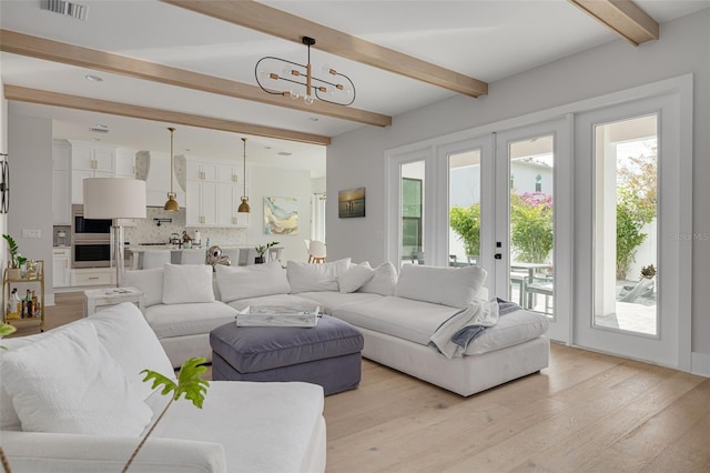 living room with french doors, a chandelier, beam ceiling, and light hardwood / wood-style flooring