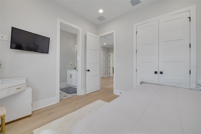 bedroom with ensuite bath, light wood-type flooring, and a closet