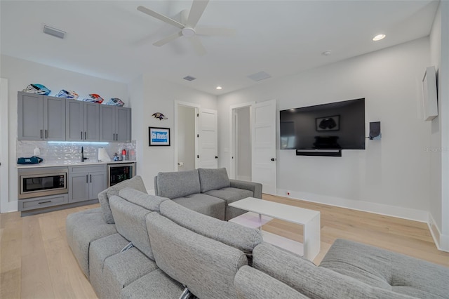 living room featuring ceiling fan, wine cooler, bar, and light wood-type flooring