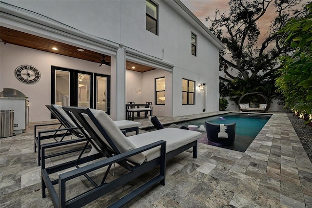 pool at dusk featuring ceiling fan, a patio area, and an outdoor kitchen