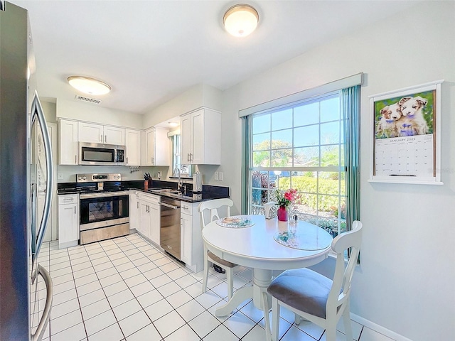 kitchen with appliances with stainless steel finishes, light tile patterned floors, white cabinetry, and sink