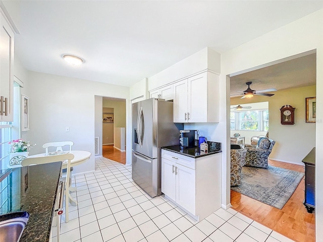 kitchen featuring stainless steel fridge, light tile patterned floors, white cabinetry, and dark stone countertops